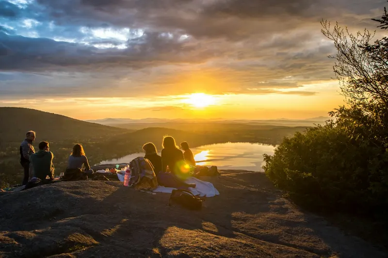 Friends watching the sunset over a lake from a rocky hilltop
