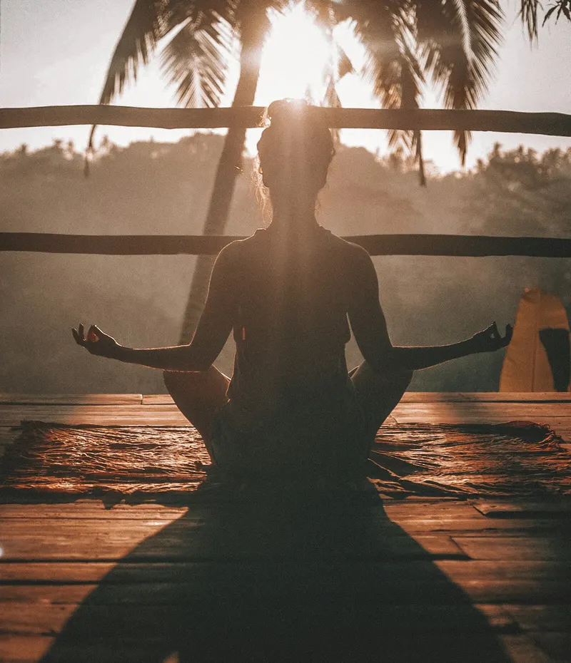 A person meditating on a deck at sunrise