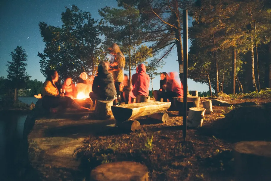 Friends gathered around a campfire among the pines at dusk
