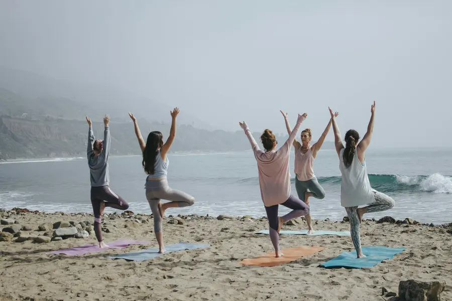 A group doing tree pose together on the beach